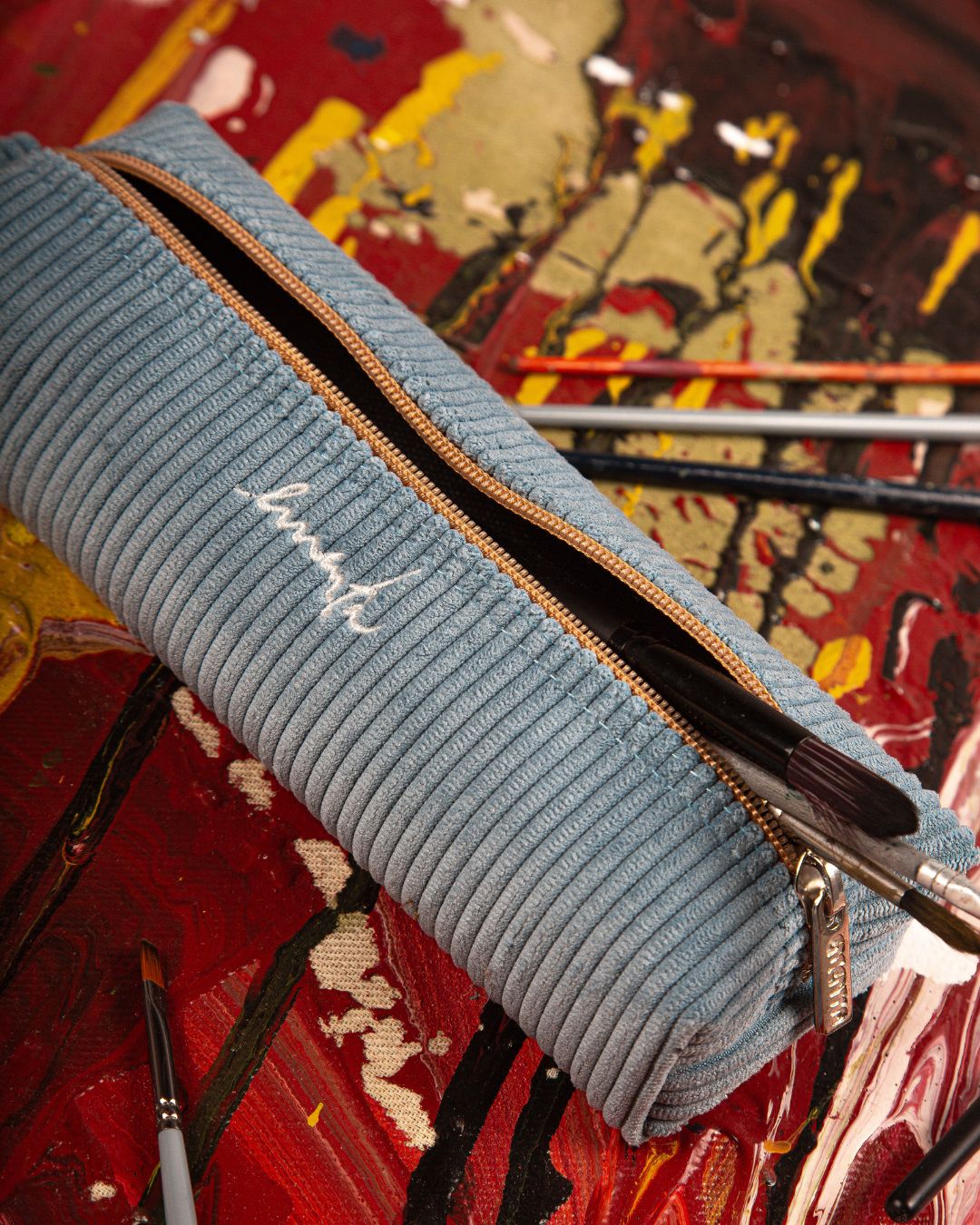 This pencil case is made from corduroy fabric and features an embroidered signature logo. It has ample space for pens, pencils, and other stationery essentials. 