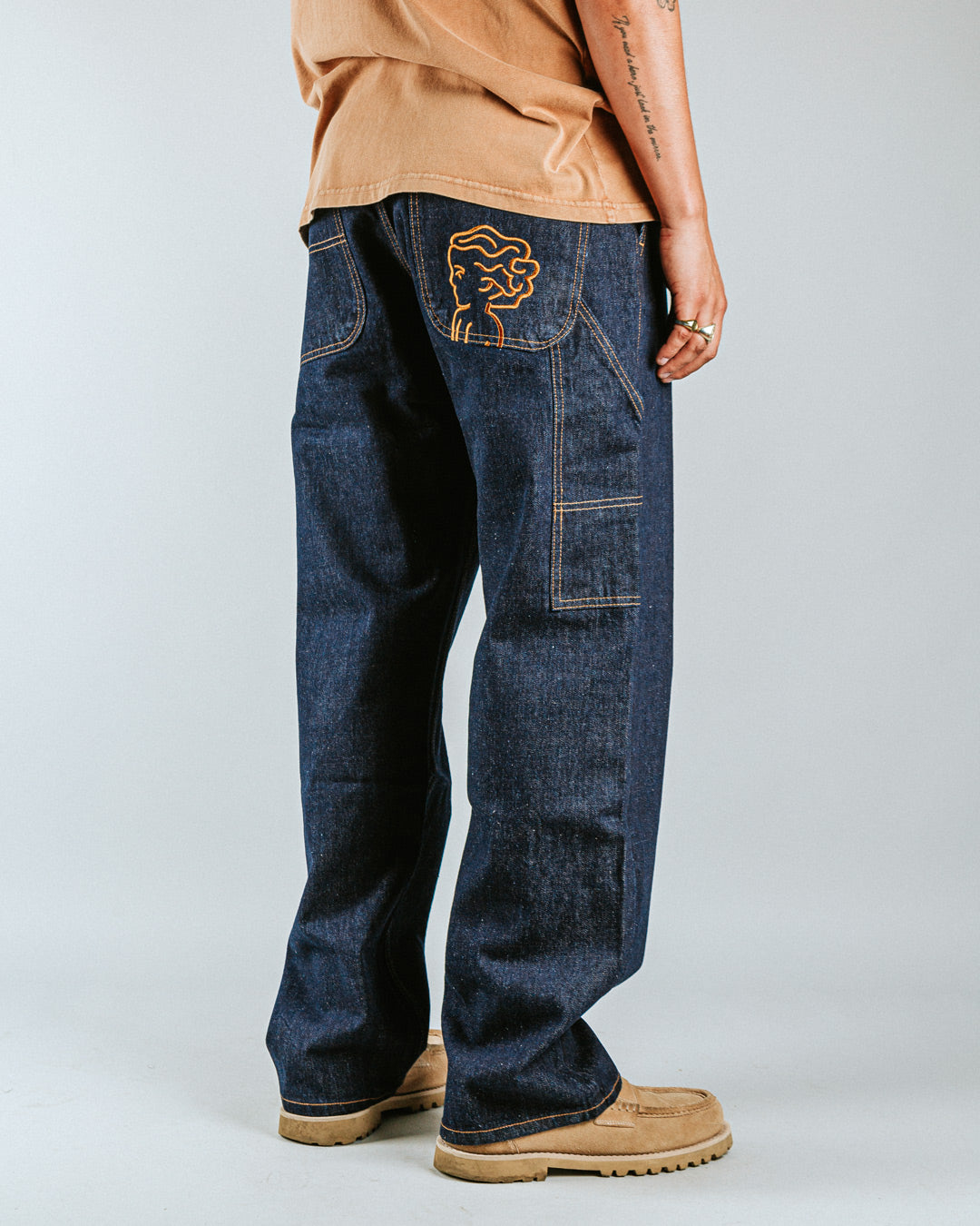 The Big Ikon Jeans Relaxed Fit Pants are designed with a baggy, relaxed straight fit and a mid-waist, offering comfort and ease of movement. The pants are crafted from blue raw denim, providing a timeless and durable look. They feature the Ikon logo embroidered in gold on the back pocket. The pants also include two front pockets, two back pockets, and one side pocket for practical storage.