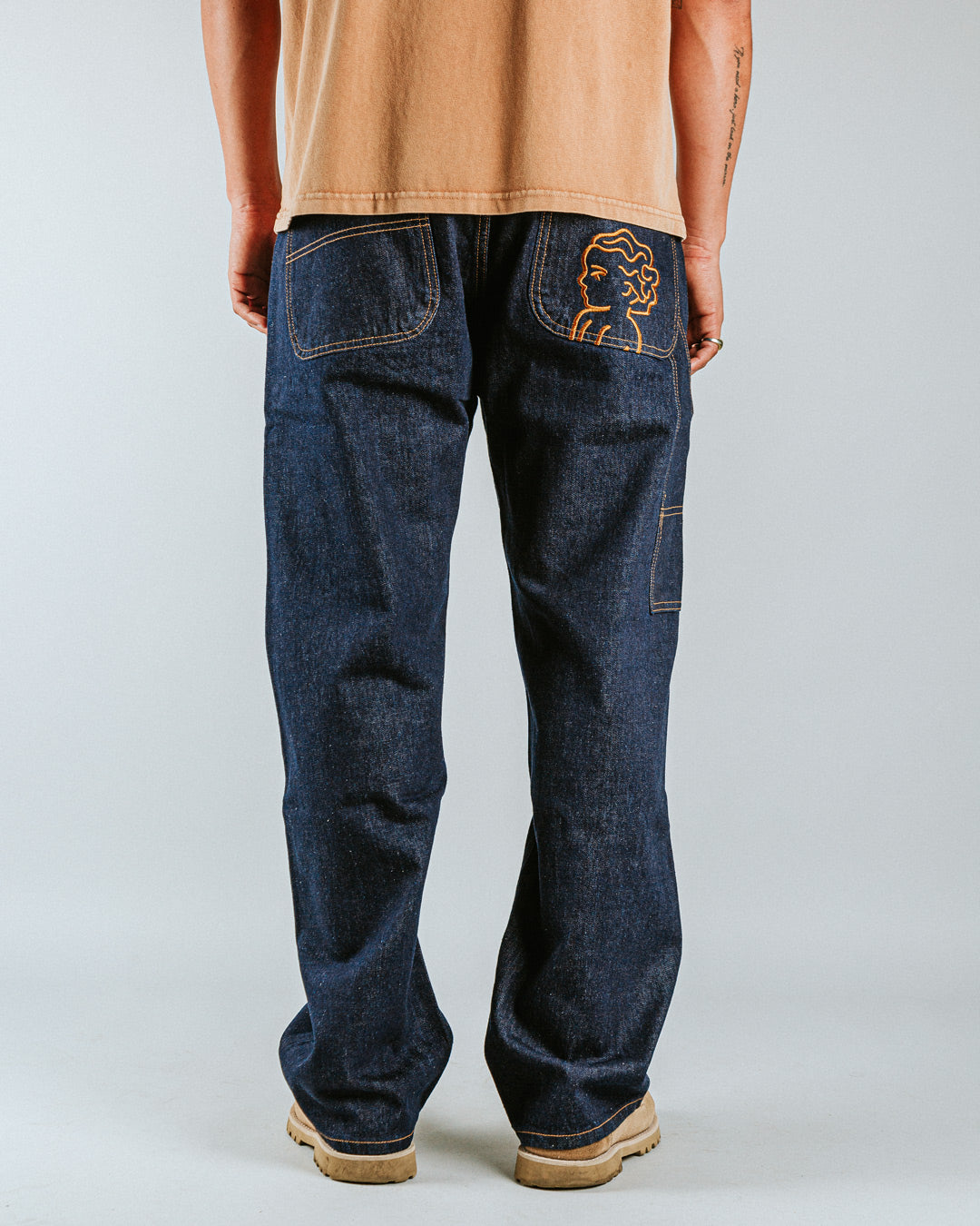 The Big Ikon Jeans Relaxed Fit Pants are designed with a baggy, relaxed straight fit and a mid-waist, offering comfort and ease of movement. The pants are crafted from blue raw denim, providing a timeless and durable look. They feature the Ikon logo embroidered in gold on the back pocket. The pants also include two front pockets, two back pockets, and one side pocket for practical storage.