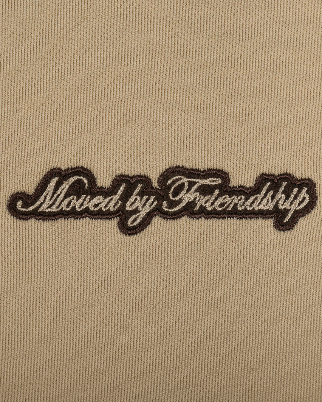 The Friendship Hoodie in camel features the motto "Moved By Friendship" embroidered on the front in a classic handwritten style. On the back, the Ikon logo appears with a dragged effect, adding a distinctive detail.
Made from heavyweight 100% cotton, the hoodie is durable and warm, with a brushed fleece interior for extra comfort. Ribbed cuffs and hem provide structure, and the kangaroo pocket adds functionality.