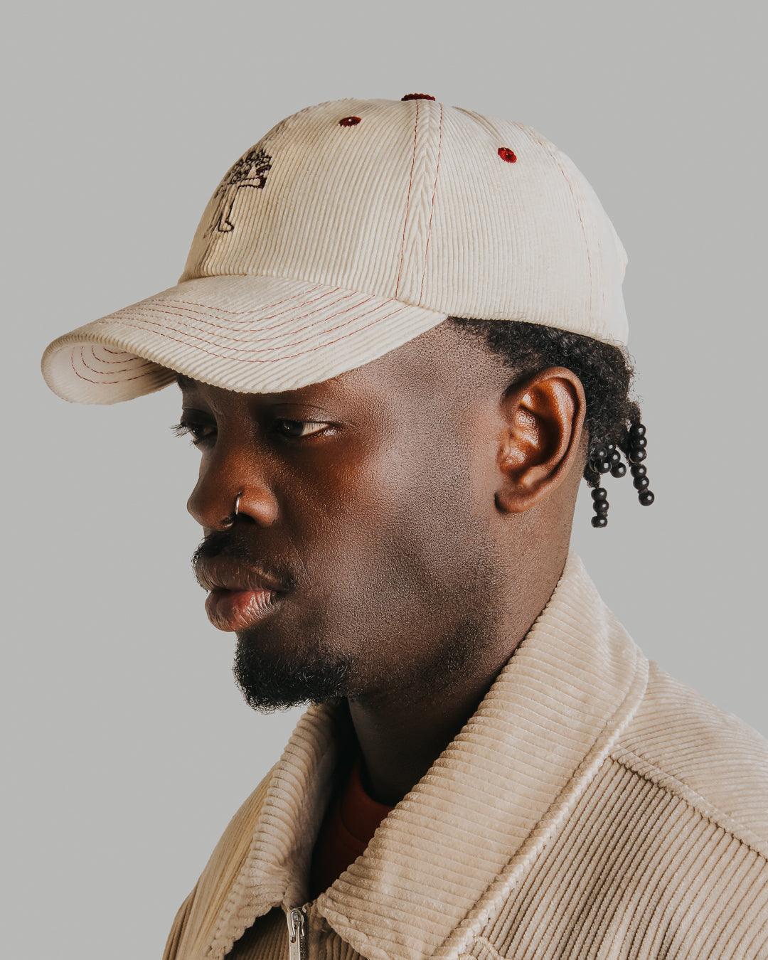 Off-white corduroy with burgundy stitching running through the seams. The Liberation design is embroidered in deep burgundy on the front, standing out against the soft texture. Six-panel build, curved brim, and an adjustable strap at the back. 100% cotton corduroy.