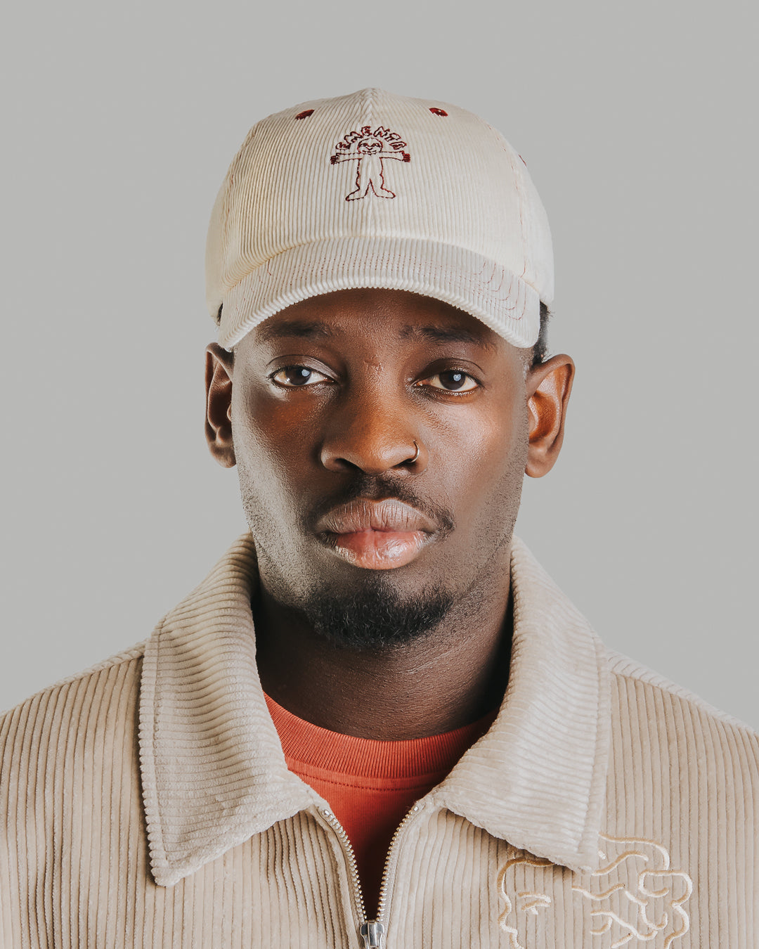 Off-white corduroy with burgundy stitching running through the seams. The Liberation design is embroidered in deep burgundy on the front, standing out against the soft texture. Six-panel build, curved brim, and an adjustable strap at the back. 100% cotton corduroy.