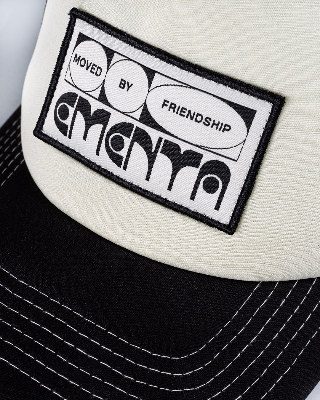 A classic breathable trucker cap featuring visible white stitching for a clean, modern look. The cap is designed for comfort and style, with an eye-catching patch that highlights out motto 'Moved By Friendship'.